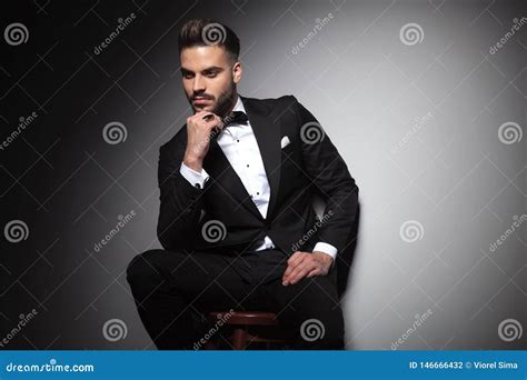 Seated Businessman In Black Tuxedo Thinking With Hand At Chin Stock