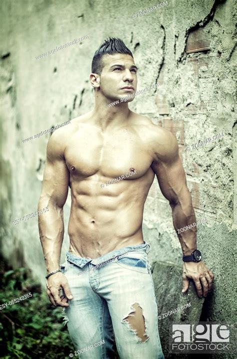 Muscular Young Latino Man Shirtless In Jeans In Front Of Concrete Wall