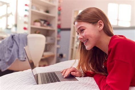 Teenage Girl Wearing Pyjamas Using Laptop Lying On Bed In Bedroom Stock