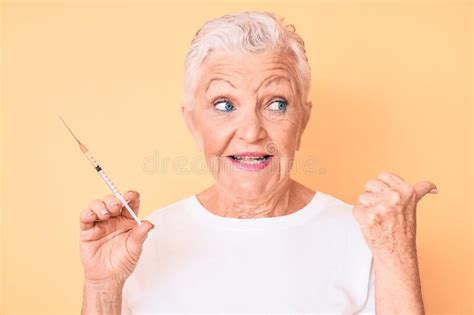 senior beautiful woman with blue eyes and grey hair holding syringe pointing thumb up to the