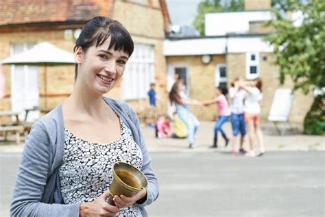 Portrait Of Teacher With Bell Supervising Break In School Playground