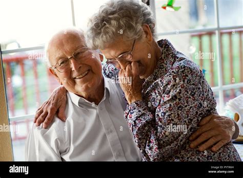 Affectionate Elderly Couple Share A Laugh As They Sit At The Kitchen