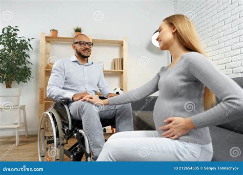 Pregnant Woman Holding A Hand Of Her Disabled Husband Sitting In A