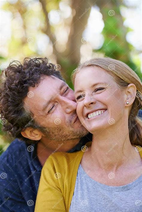 giving her a big kiss on the cheek an affectionate husband and wife standing outdoors stock