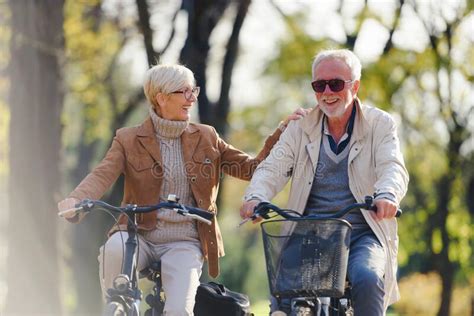 cheerful active senior couple riding bicycles in public park together having fun perfect