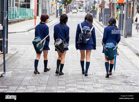 Line Of Four Japanese Schoolgirls Walking Away Along A Street With Their Backpacks Slung Over