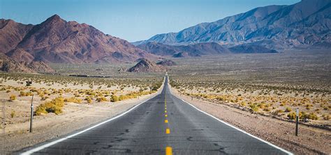 Long Straight Road In The Desert Leading Off Into The Mountains By