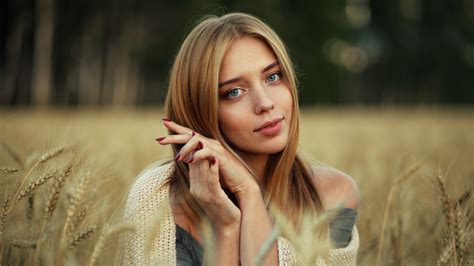 Girl Model Is Sitting In Dry Grass Field With Blur Background Posing