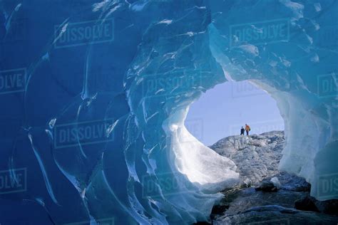 Two Hikers Peer Into The Entrance Of An Ice Cave On