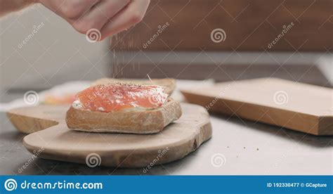 Man Hands Seasoning Smoked Salmon On Ciabatta With Cream Cheese To Make A Sandwich On Wood Board