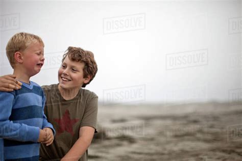 Boy Comforting His Crying Younger Brother On Beach Stock Photo