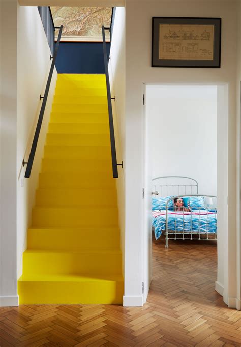 There Is A Yellow Staircase Leading To The Bedroom In This House With White Walls And Wood Floors