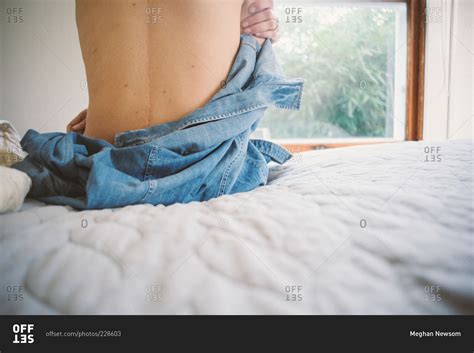 A Woman Taking Off Her Shirt While Siting On The Edge Of A Bed Stock Photo Offset