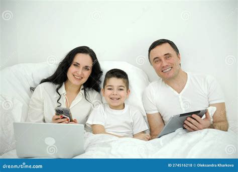 Familia E Hijo Mirando Y Jugando Al Tablet En La Cama Foto De Archivo