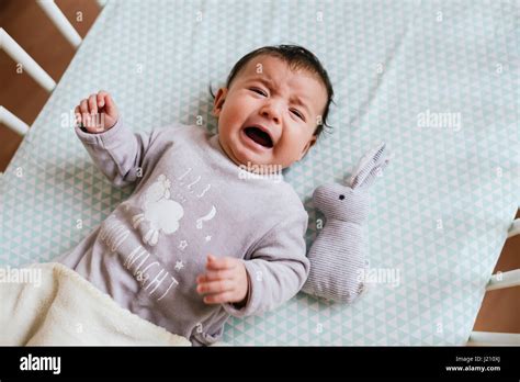 Portrait Of Crying Baby Girl Lying In Crib With Toy Bunny Stock Photo