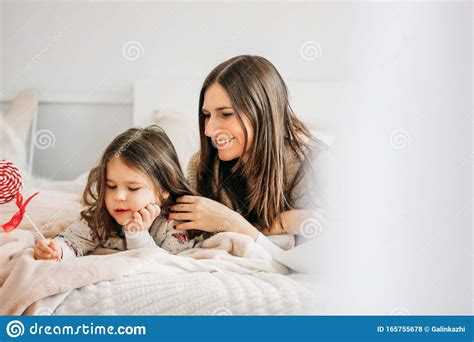 Madre Joven Sonriente E Hija Con Caramelos En La Cama En Casa Foto De