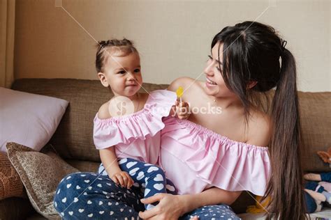 Picture Of Young Mother Sitting On Sofa With Her Little Daughter Indoors Looking Aside Royalty