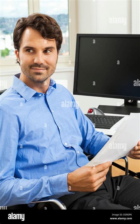 Young Handsome Man Sitting At His Desk In The Office While Reading