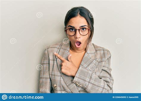 Young Brunette Woman Wearing Business Jacket And Glasses Surprised Pointing With Finger To The