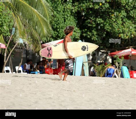 A Young Indonesian Man Walking Down The Beach And Carrying A Surboard