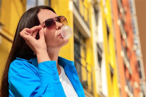 Beautiful Young Woman With Sunglasses Blowing Chewing Gum On City