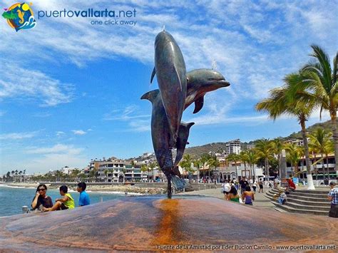 A Statue Of Two Dolphins On Top Of A Rock Near The Ocean With People