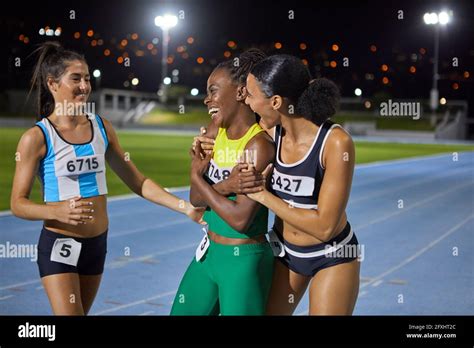 Happy female track and field athletes celebrating and hugging on track