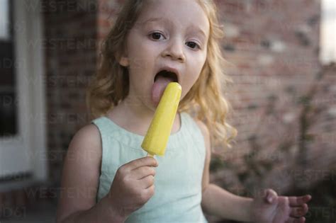 Portrait Of Girl Eating Popsicle Stick While Standing Against House