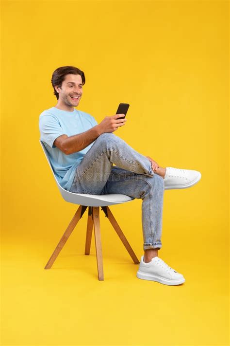 Happy Guy Using Cell Phone At Studio Sitting On Chair Stock Image