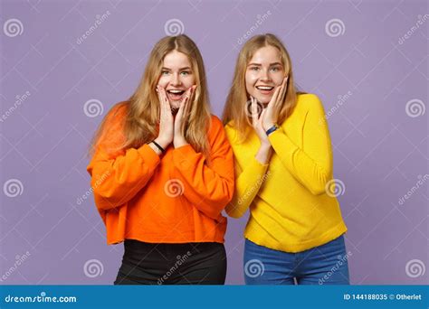 Two Surprised Young Blonde Twins Sisters Girls In Vivid Colorful Clothes Putting Hands On Cheeks