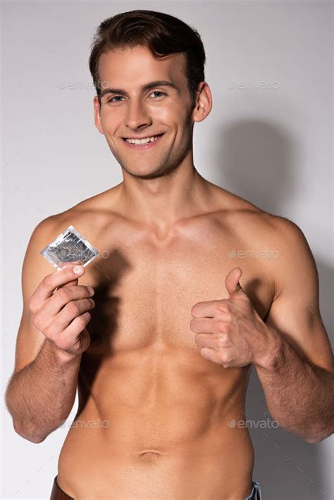 Cheerful And Muscular Man Showing Thumb Up While Holding Condom On White Stock Photo By