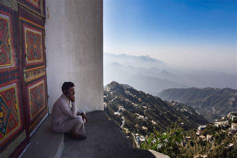 A Man Sitting On The Side Of A Building Next To A Wall With Mountains