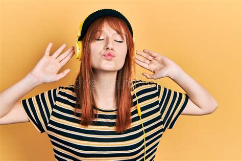 Redhead Young Woman Listening To Music Using Headphones Looking At The