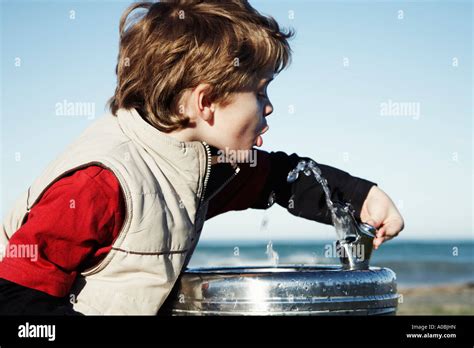 Young Boy Drinking From Water Fountain Bubbler With Blue Sky Behind