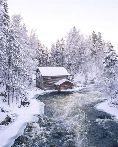 A River Running Through A Snow Covered Forest Next To A Log Cabin In