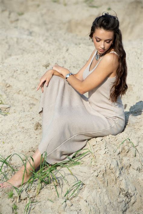 Beautiful Young Woman In Elegant Dress Sitting On The Beach At Sunset