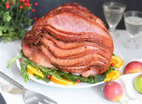 a large ham sitting on top of a white plate next to fruit and silverware