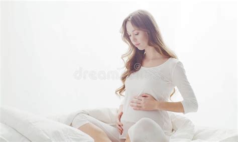 Happy Pregnant Woman Touching Her Beautiful Belly Sitting In The Bed