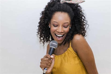 Cheerful Young Woman Singing While Holding Microphone Against White