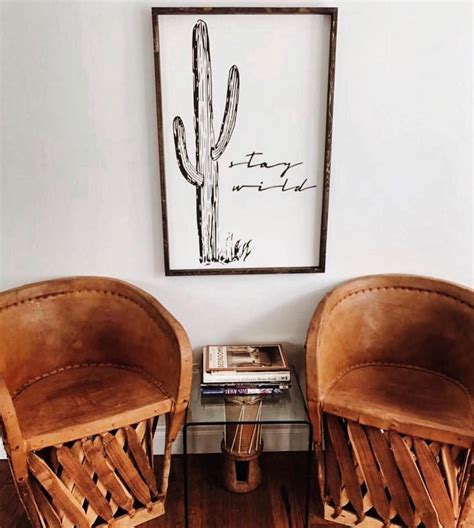 Two Chairs Sitting Next To Each Other In Front Of A Framed Cactus Print