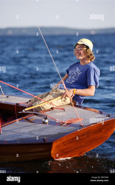 A Smiling Teenage Boy At The Helm Of A Classic Wooden Sailing Dinghy