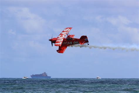 a red plane flying over the ocean with a boat in the background