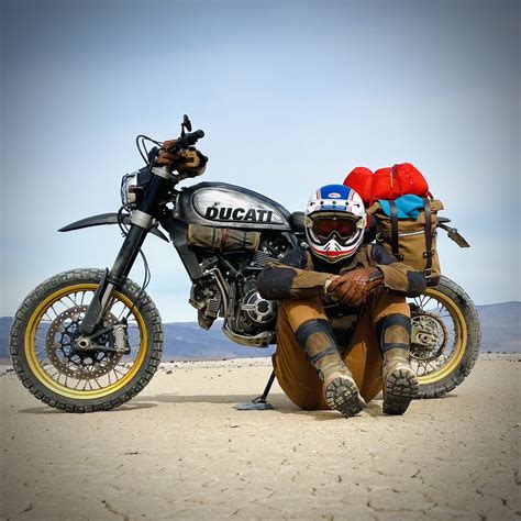 A Man Sitting On The Ground Next To A Motorcycle With Two Bags On His Back