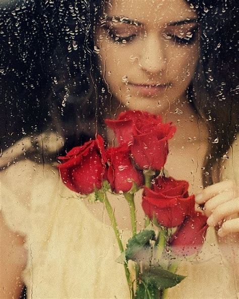 A Woman Holding Two Red Roses In Front Of A Rain Soaked Window With