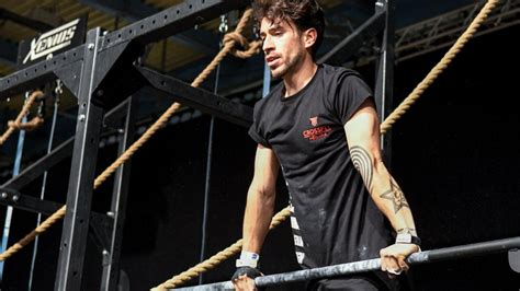 A Man With Tattoos On His Arm Holding Onto A Bar In Front Of Ropes At A