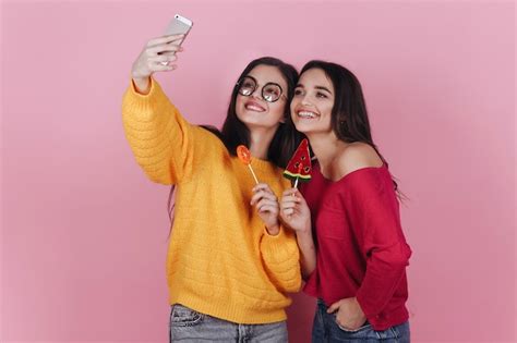Free Photo Two Smiling Girls Take Selfie On Their Phones Posing With Lollipops