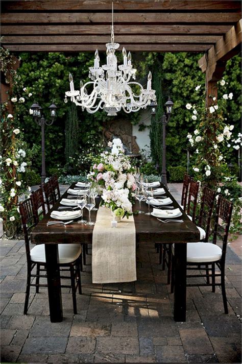 An Outdoor Dining Table With White Flowers And Chandelier Hanging From