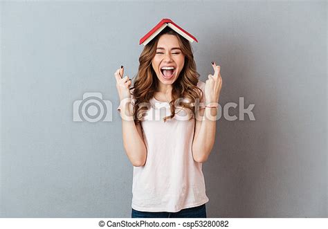 Portrait Of A Cheerful Happy Woman Holding Book On Her Head With Crossed Fingers For Good Luck