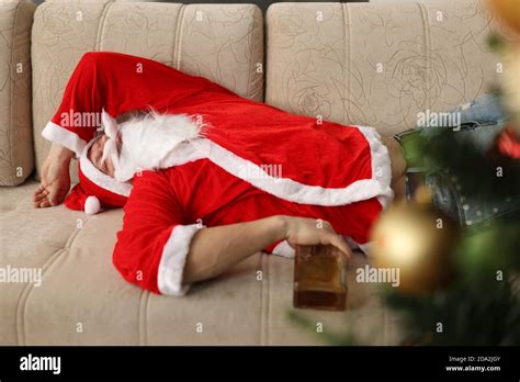 Drunk Santa Claus Is Sleeping On Couch With Bottle Of Whiskey In Hands