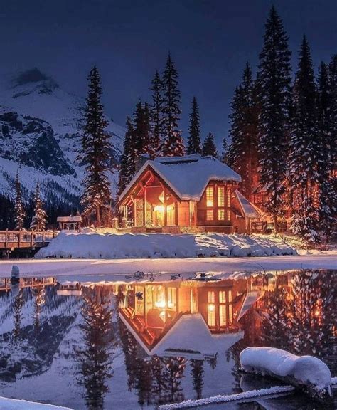 A Cabin Is Lit Up At Night In The Snow With Trees Around It And Lights On